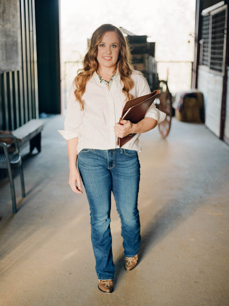 Lindsay Lucas standing in a horse barn, holding a leather binder.
