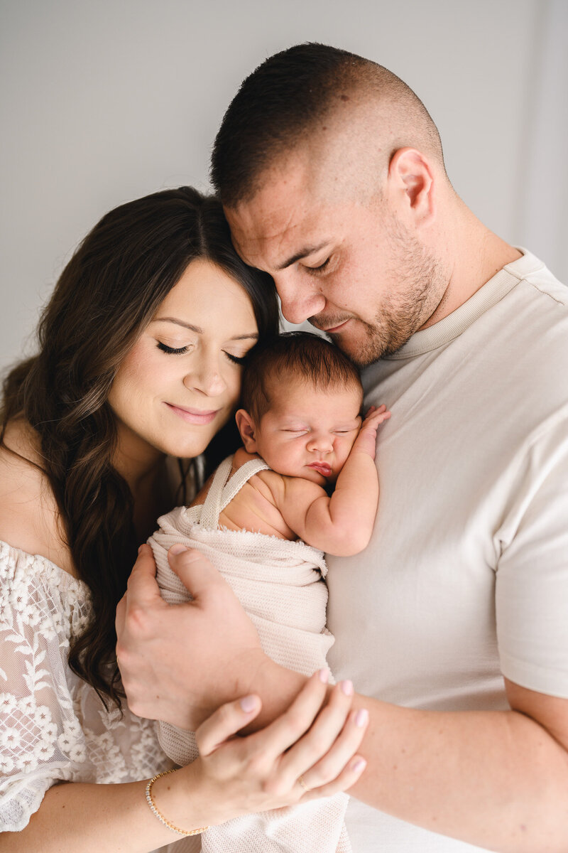 Parents smiling proudly at newborn baby girl sleeping in front of them. 