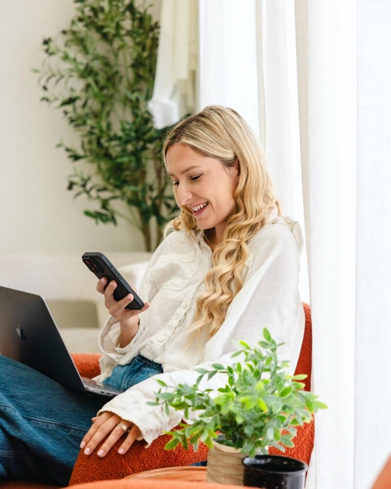 social media virtual assistant on her phone sitting on an orange chair