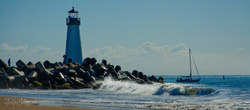 Sailboat sets out for an afternoon cruise leaving Santa Cruz Harbor, passing Walton Lighthouse out to Monterey Bay.