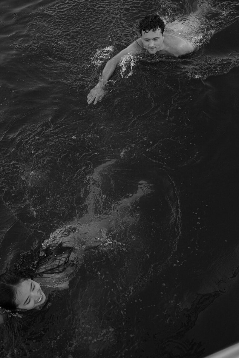 A black and white image of two people swimming in open water.