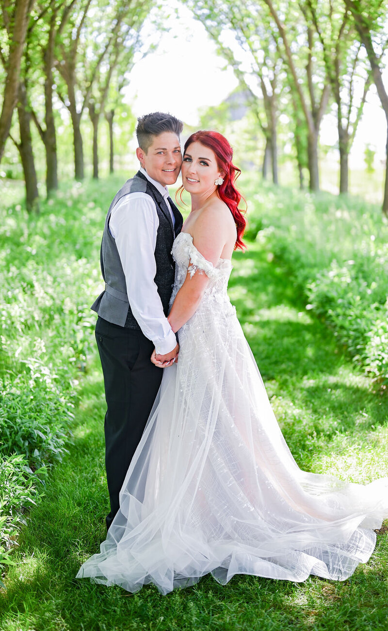 Portrait of two brides in a green tree alley.