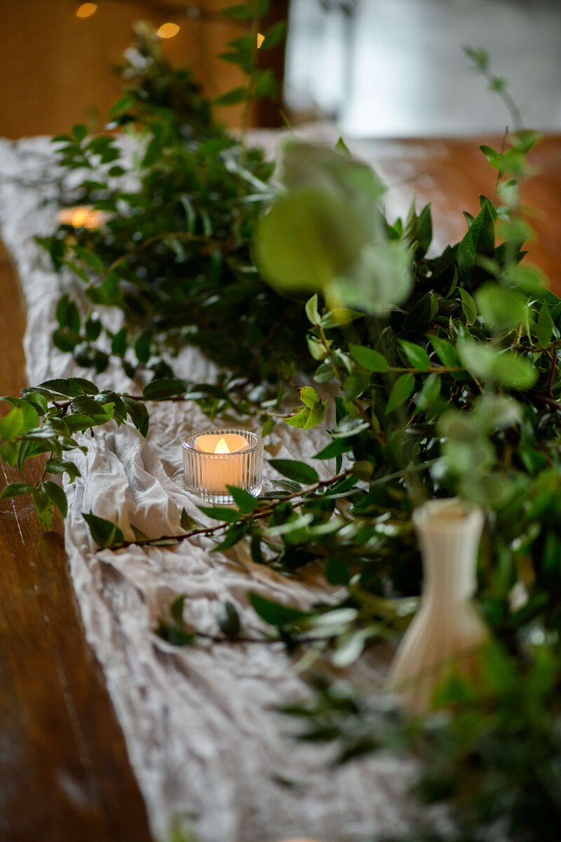 Tea lights twinkle among greenery in a close-up of wedding reception decor