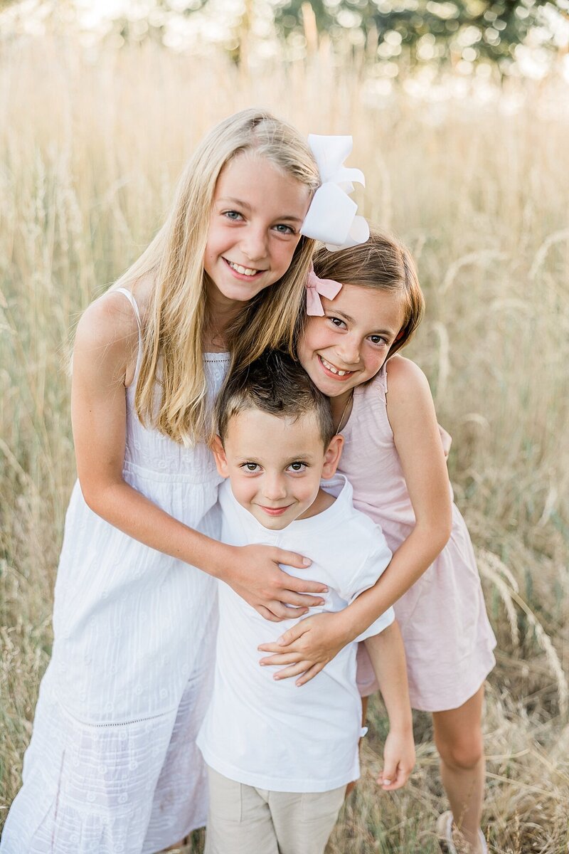 Three kids hugging in Portland Area Field by Ann Marshall Photogrpahy