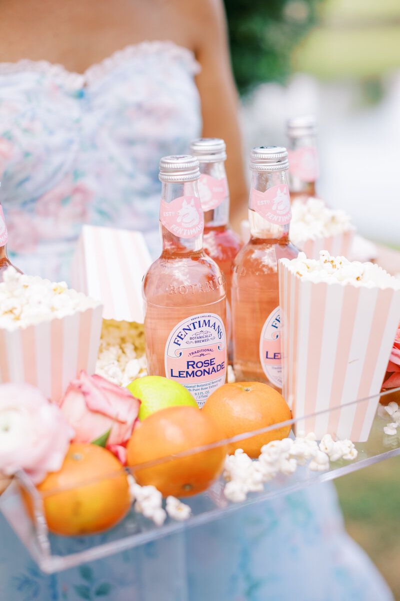 Eleanor Stenner in blue dress holding tray of fruit, popcorn, bottled lemonade, and flowers