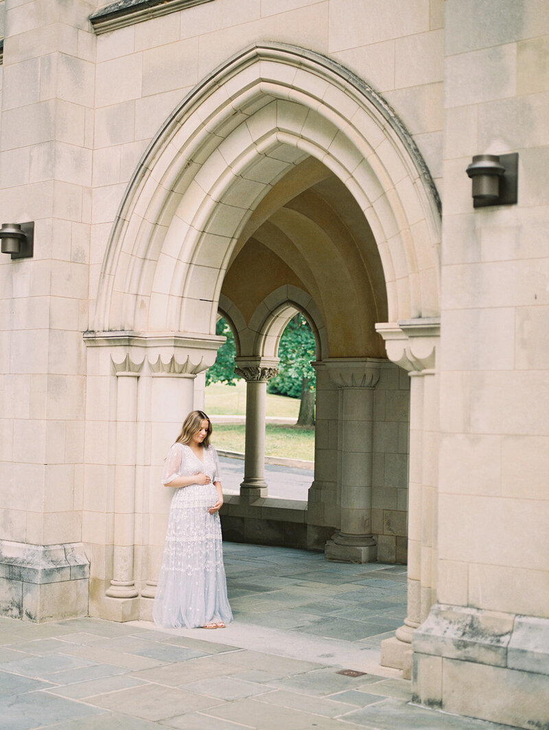 Mother with brown hair leans against stone archway, photographed by Maryland maternity photographer Marie Elizabeth Photography.