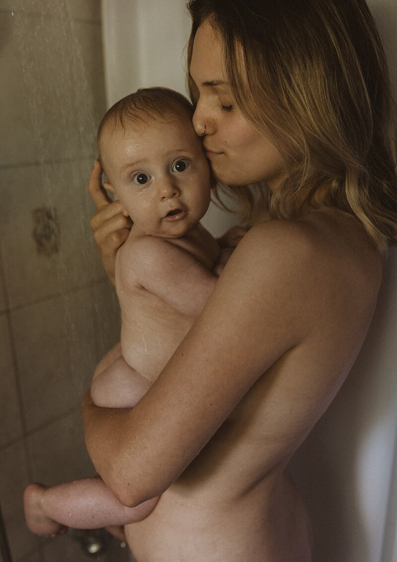 Eine Mutter steht mit ihrem Kind in der Dusche und gibt dem Kind einen Kuss auf die Stirn.