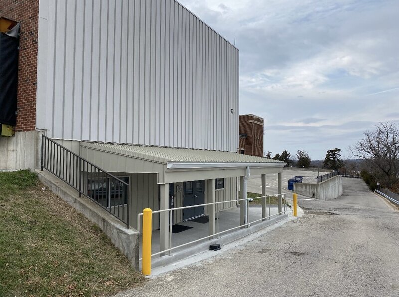 Steel awning with protective railing and yellow safety bollards installed on a commercial building entrance.