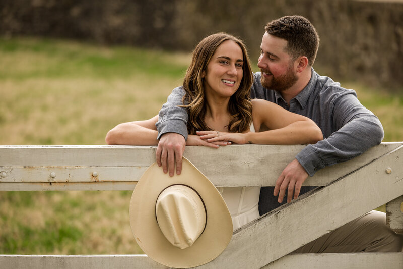 Couple leaning on a rustic fence with a cowboy hat at Valley Forge National Historical Park, enjoying the outdoors.