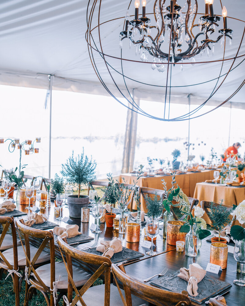 A rustic wedding in a marquee with a large round light chandelier and copper accents and wooden cross back chairs
