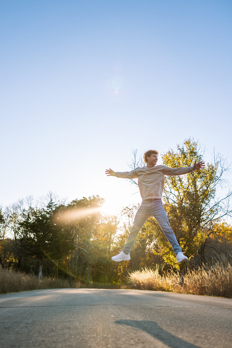 Senior guy jumping in the air with the golden sunset behind him in Missouri. 