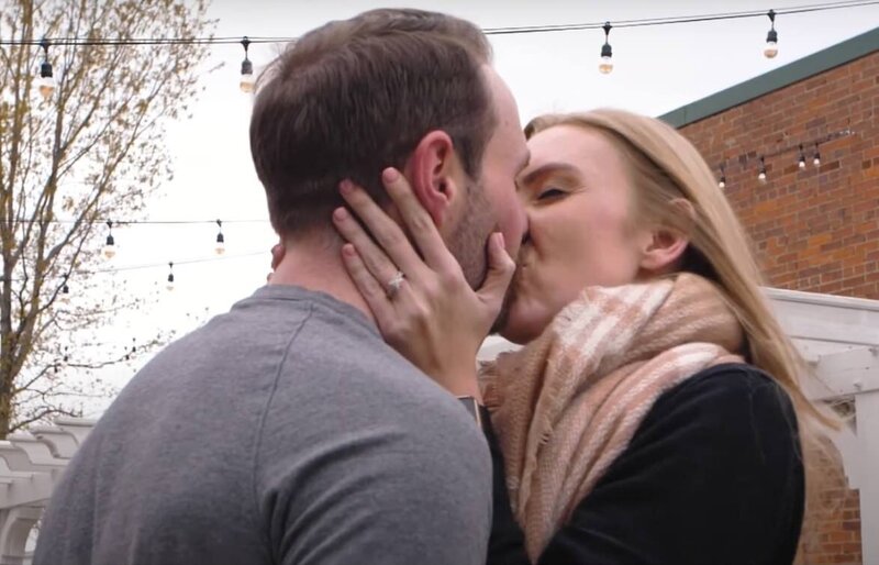 A couple kissing and showing off an engagement ring 