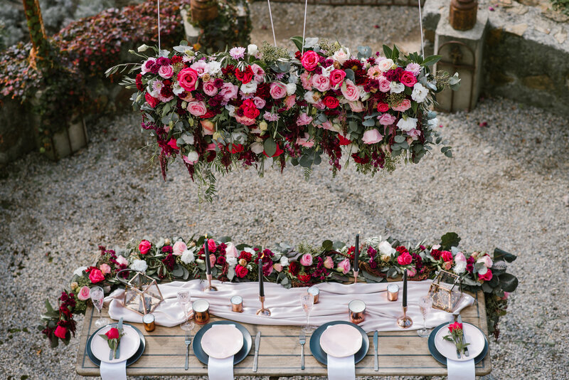 Red floral canopy chandelier above wedding reception table with red and pink roses
