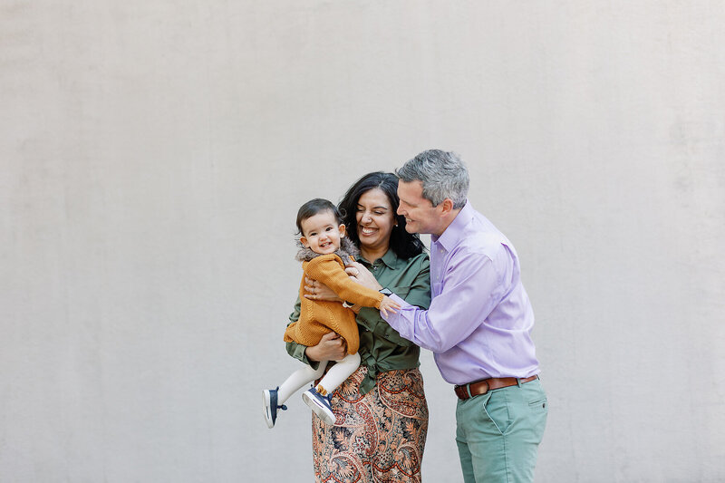 A couple holds their little girl while smiling.