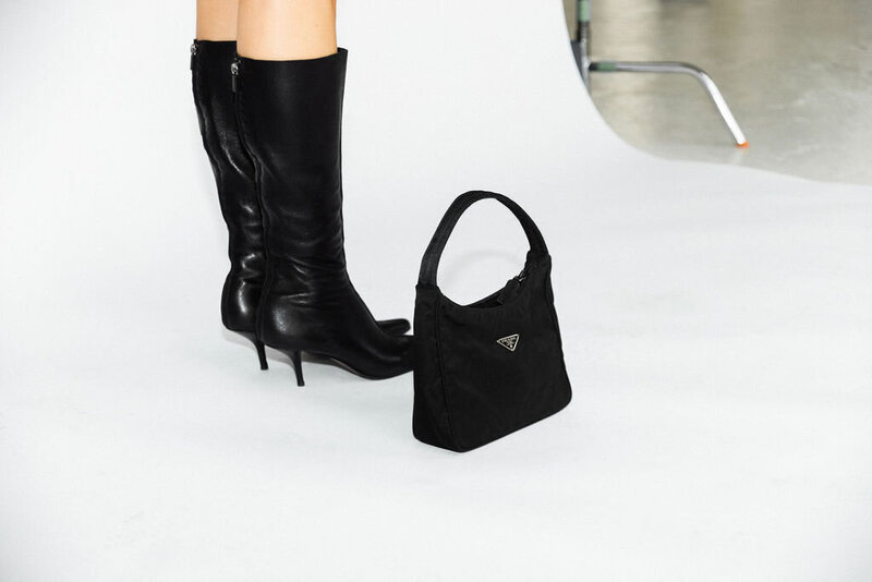 Black designer boots next to a fashionable handbag on a white floor