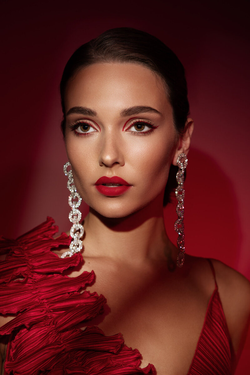 Bold portrait of Luciana Cid in a red outfit with dramatic earrings and strong makeup, captured by Ylva Erevall.