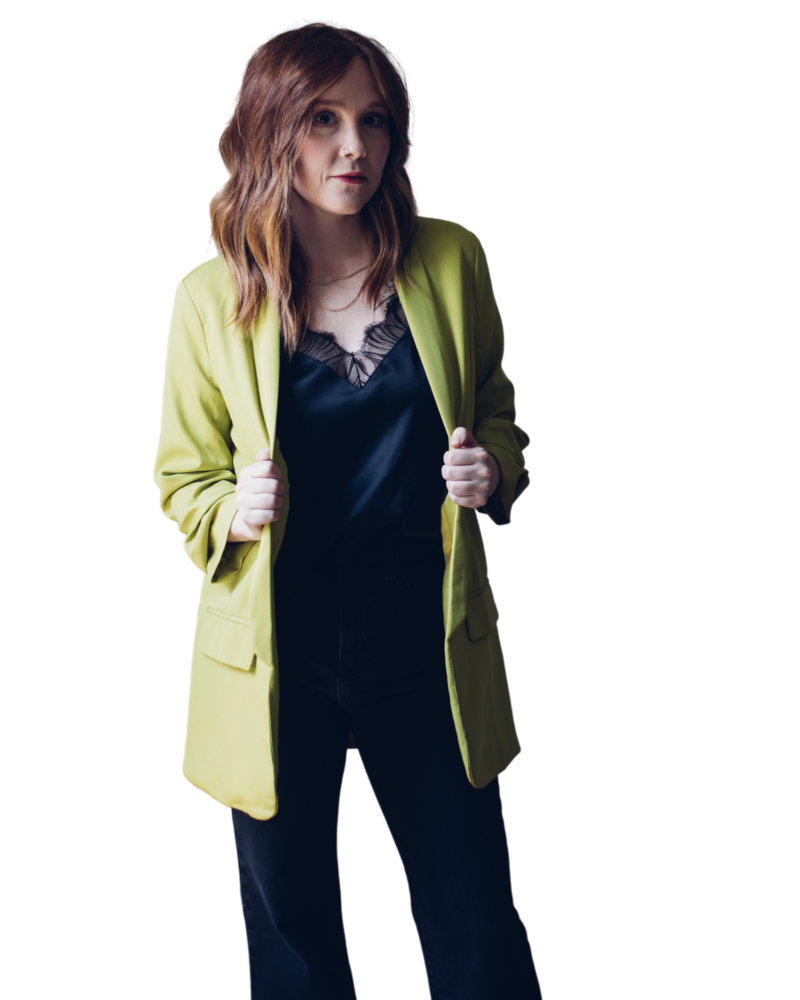 A person with medium-length, wavy hair stands facing forward, wearing a lime green blazer over a black top. They hold the blazer lapels with both hands, ready to shine in their wedding photography SEO campaign.