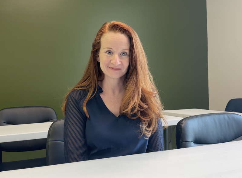 Jennifer sitting in a classroom, smiling warmly in front of a green wall — instructor headshot style