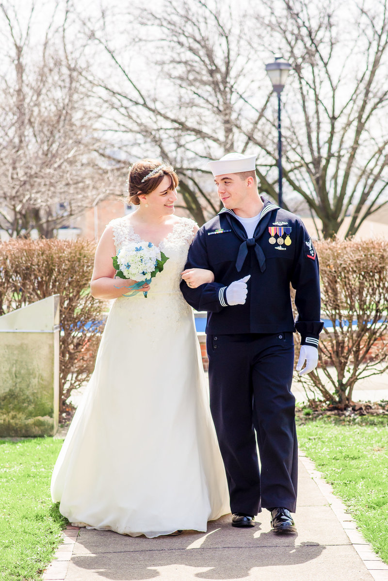 A navy groom escorts his bride down the sidewalk