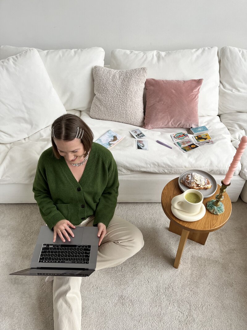 An overhead image of Margarita, a website copywriter sitting on the floor smiling at her laptop screen.