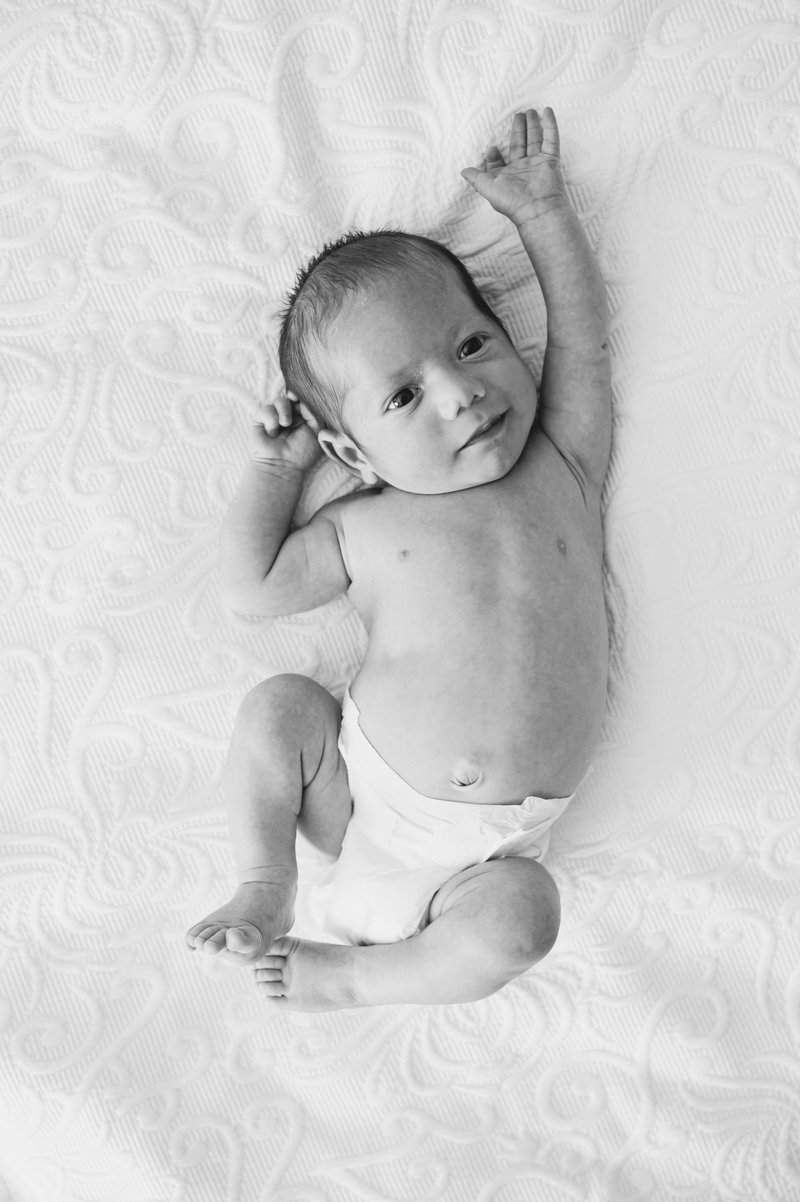 Black and white photo of a newborn baby as he squirms on the bed wearing a nappy.