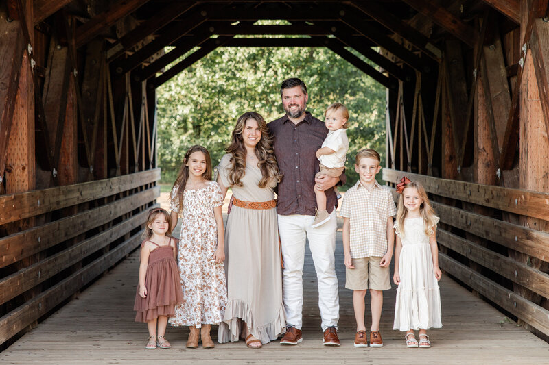 Family of seven posed and smiling in a barn walkway.