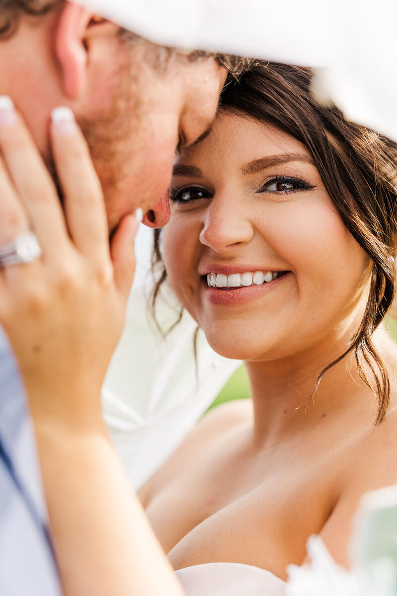 Close up of bride cupping her groom's face and smiling at camera