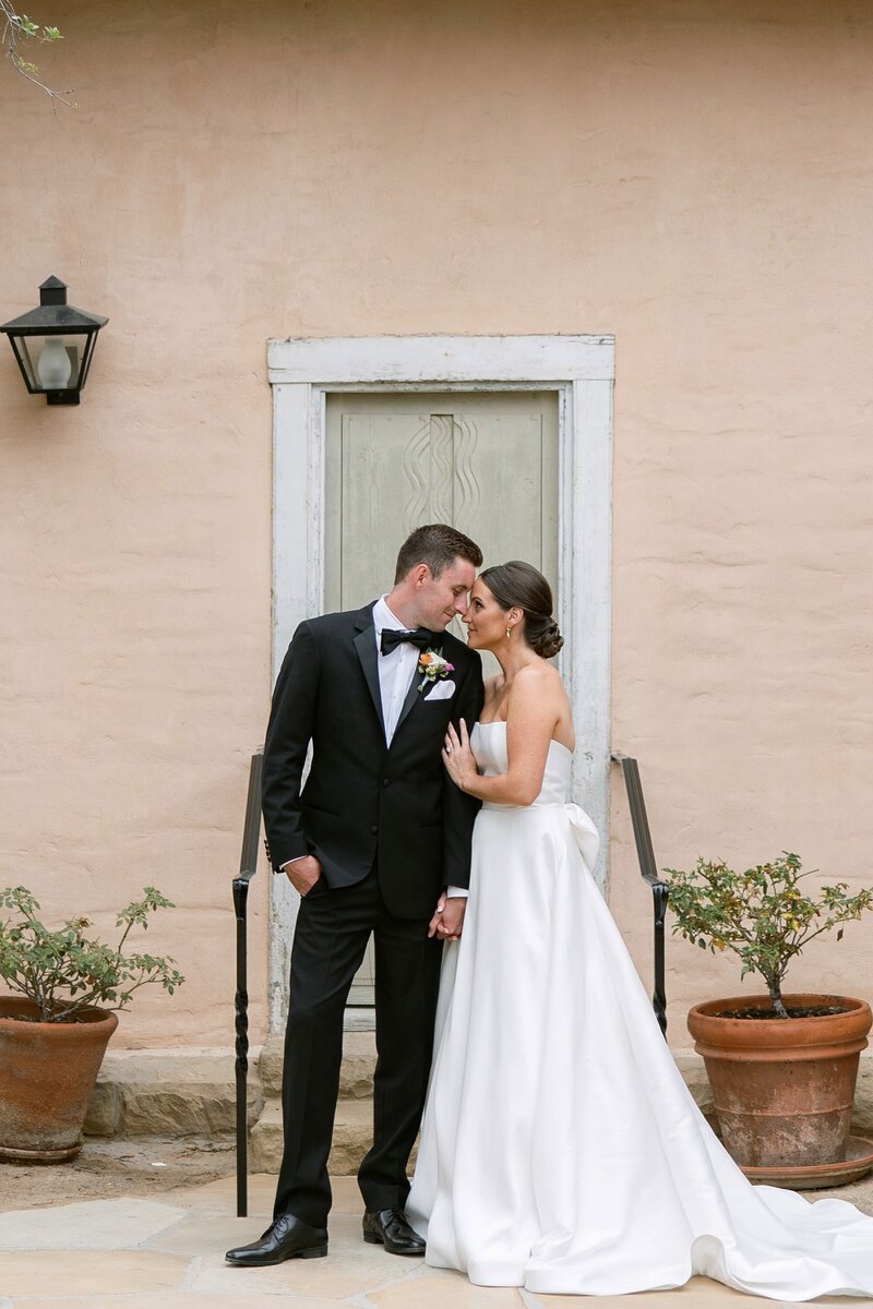 Bridal party looks on as bride and groom kiss under clear umbrellas