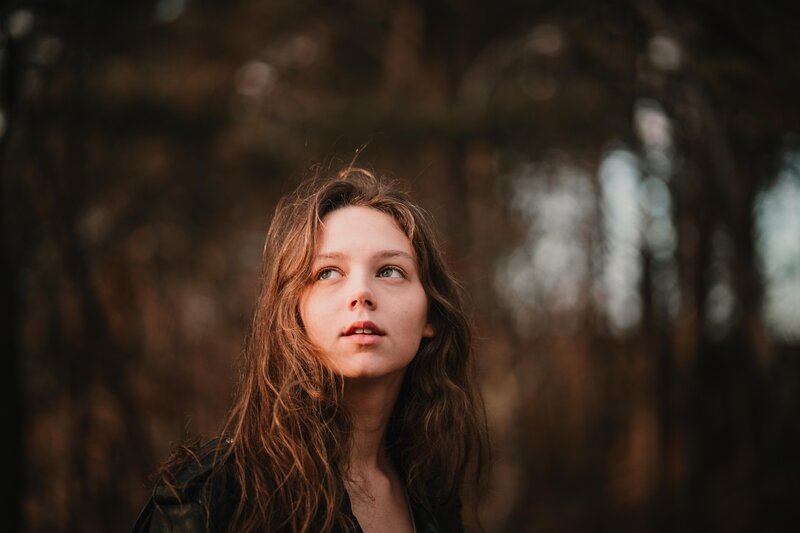 Model stands in the sunlight with the woods in the background.