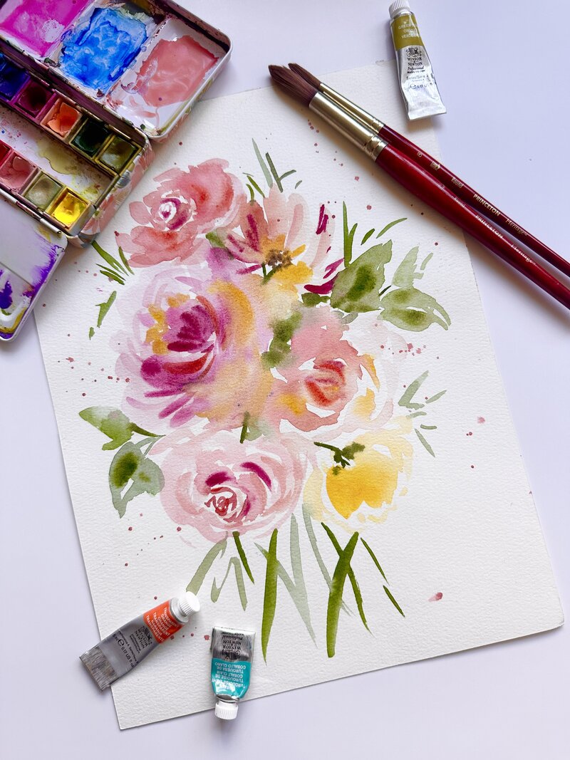 Colorful watercolor painting of roses and blooms next to paint palette and paint brushes