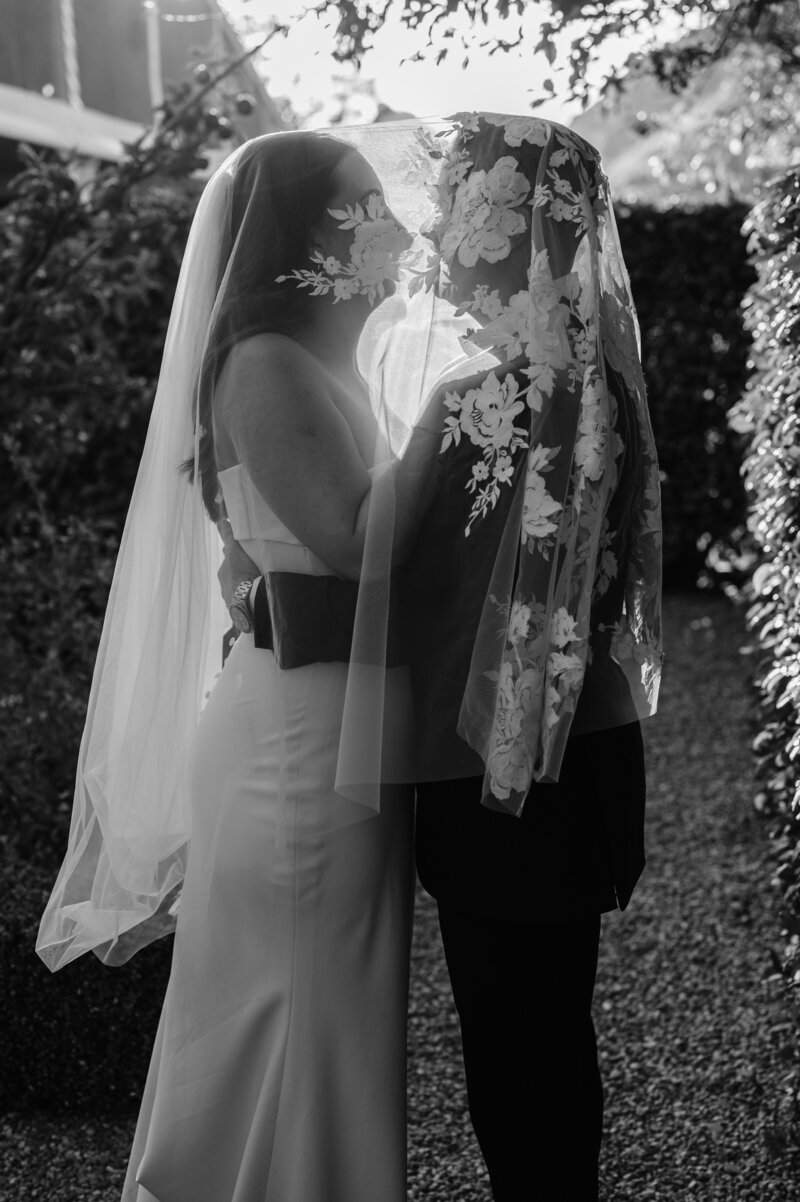 black and white shot of bride and groom under a lace veil in the sunset at the winehouse in new zealand