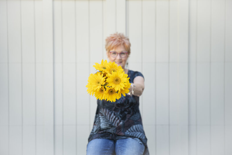 Jane Shine, smiling into the camera holding a bouquet of sunflowers out
