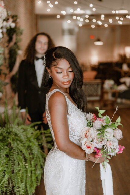 Bride holding a lush flower bouquet with a groom in a tuxedo faded into the background