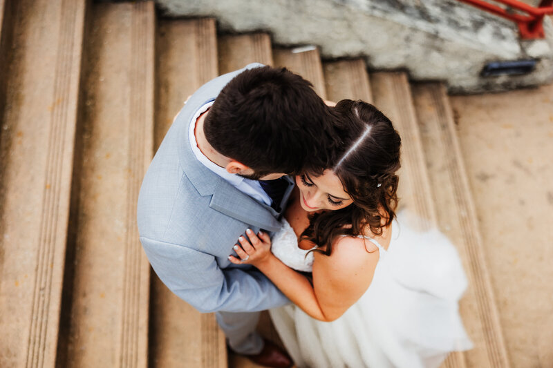 A groom snuggles into his brides forehead on a staircase.