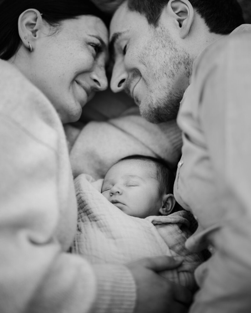 New parents snuggle together on a blanket with their newborn baby between them