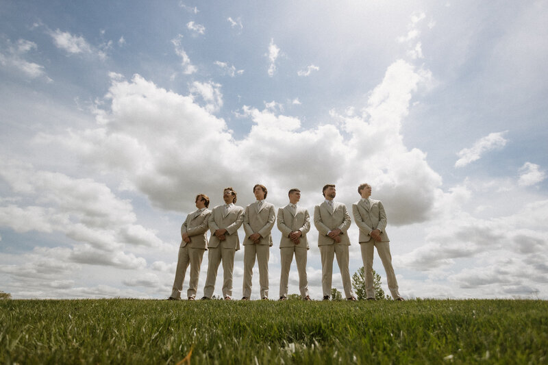 A group of groomsmen standing confidently beneath a bright sky, captured by Daniel from Rainstorm Photo & Video in a modern, cinematic style.