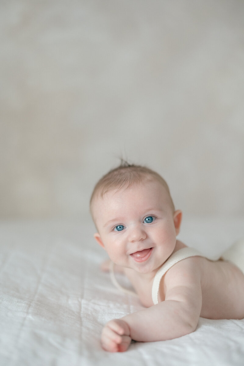 Baby boy doing tummy time in a romper on a bed with a lime washed wall behind him by NJ Newborn Photographer