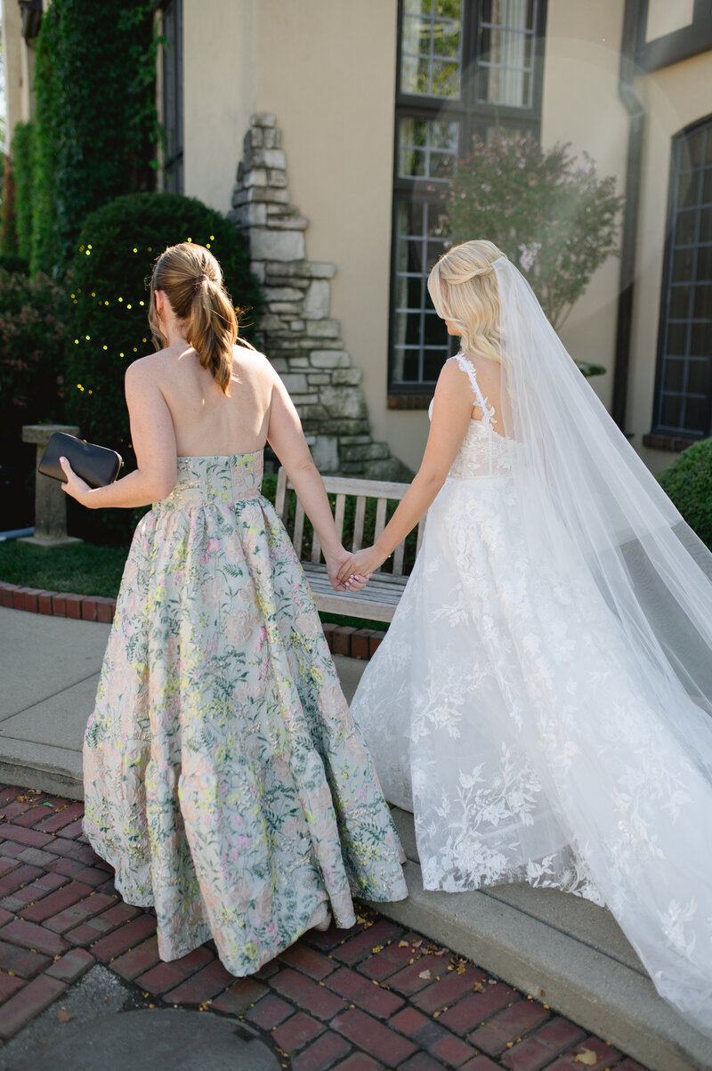 Bride and bridesmaid holding hands walking away from the camera
