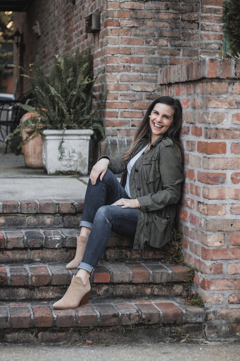 Katelin sitting on brick steps leaning against a brick support smiling.