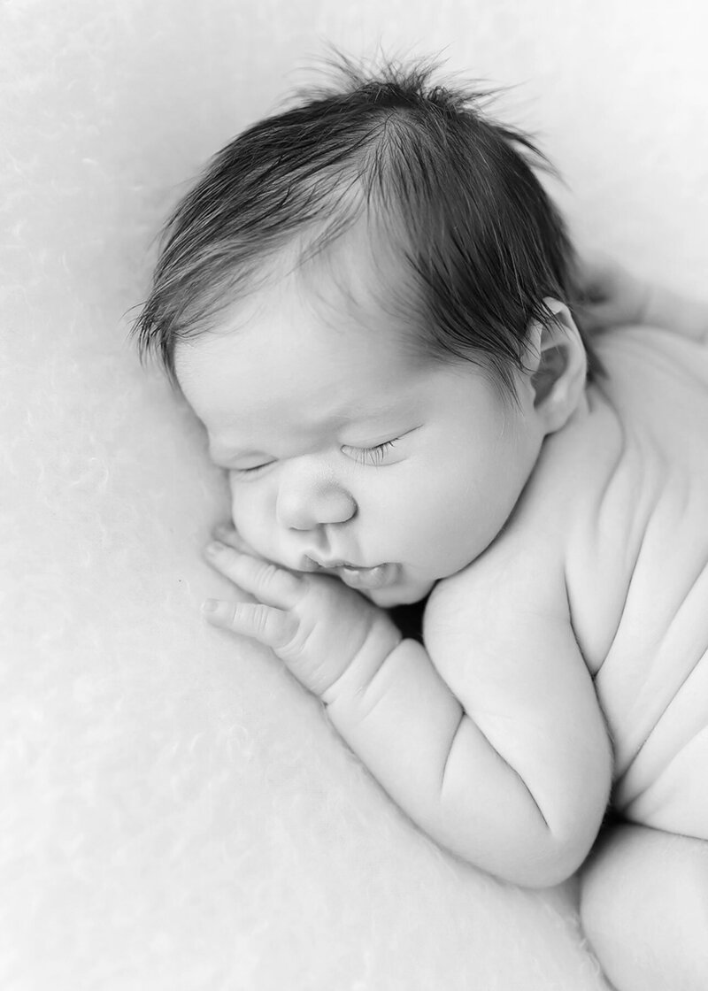 Baby with lots of dark hair lays curled up on his tummy, with lots of wrinkly rolls on his back