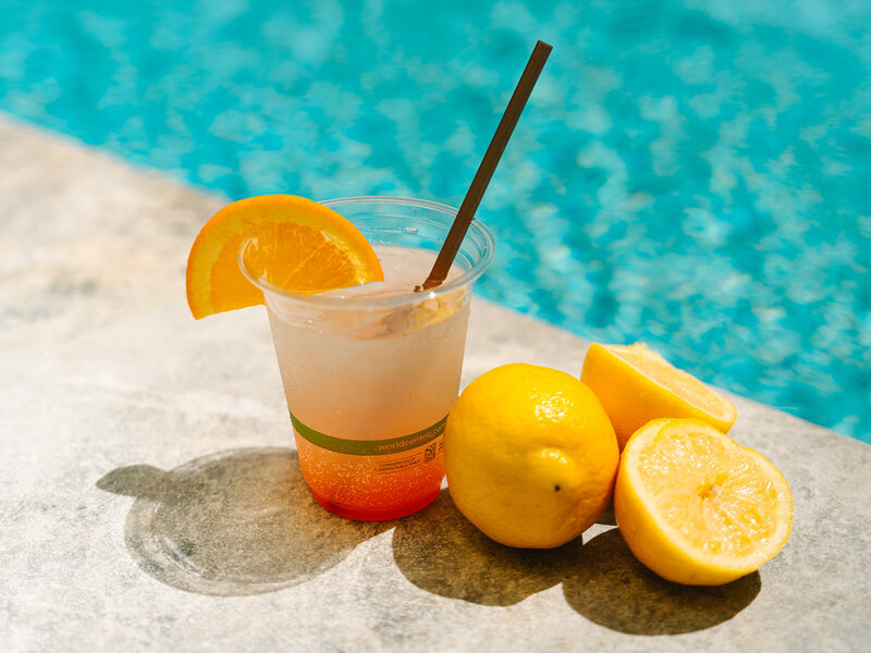 Drink with orange slice on the rim sitting next to lemons by the pool