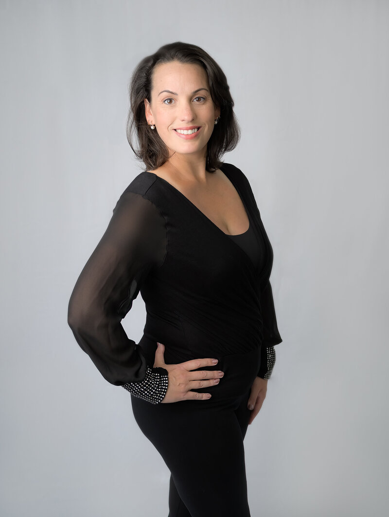 Head shot of photographer Beth Benecki dressed in black standing in front of a light gray background.