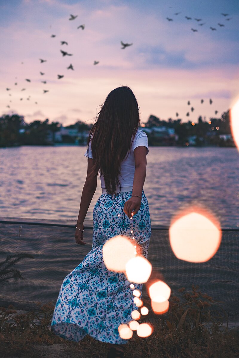 Woman walking towards water holding string of lights