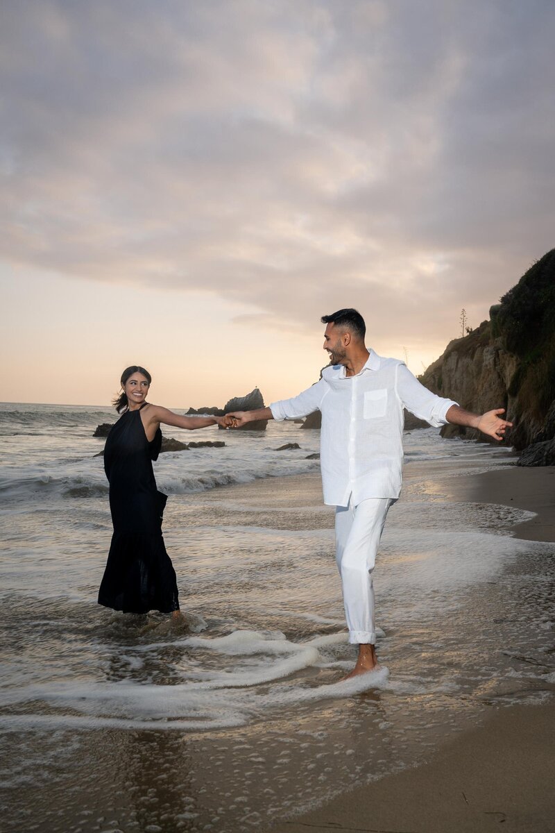 Indian couple eloping at El Matador State Beach in Malibu celebrating and dancing at sunset with rocky beach waves.