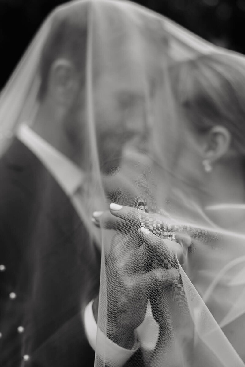Bride and groom clasp hands under wedding veil