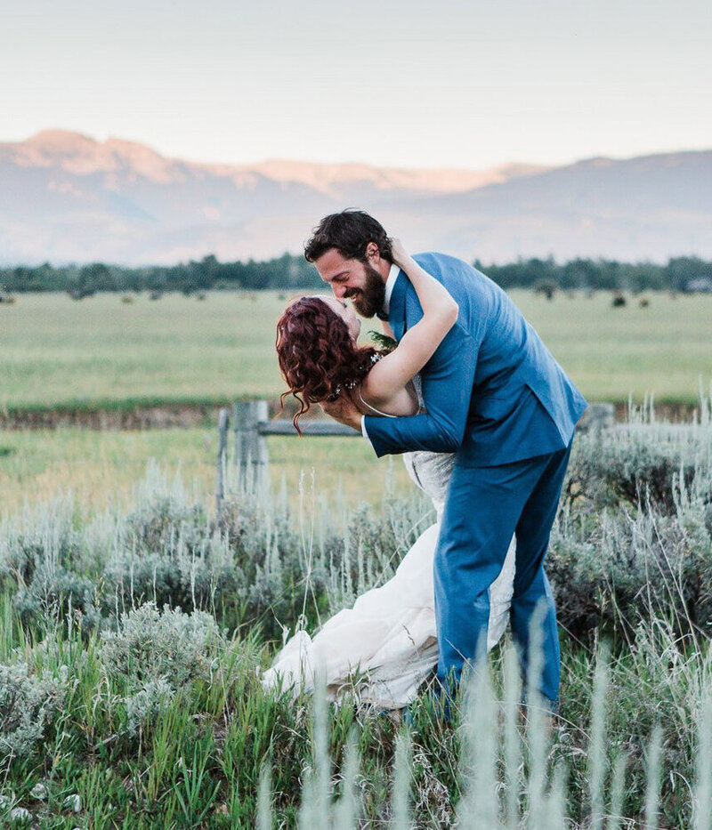 A groom dips his bride in a sagebrush field outside of Grand Teton National Park