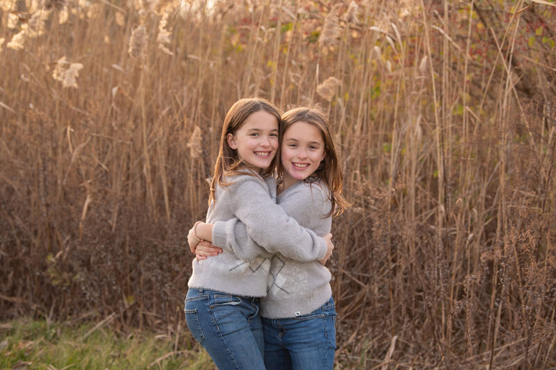 Twin girls hugging each other at a park during sunset.
