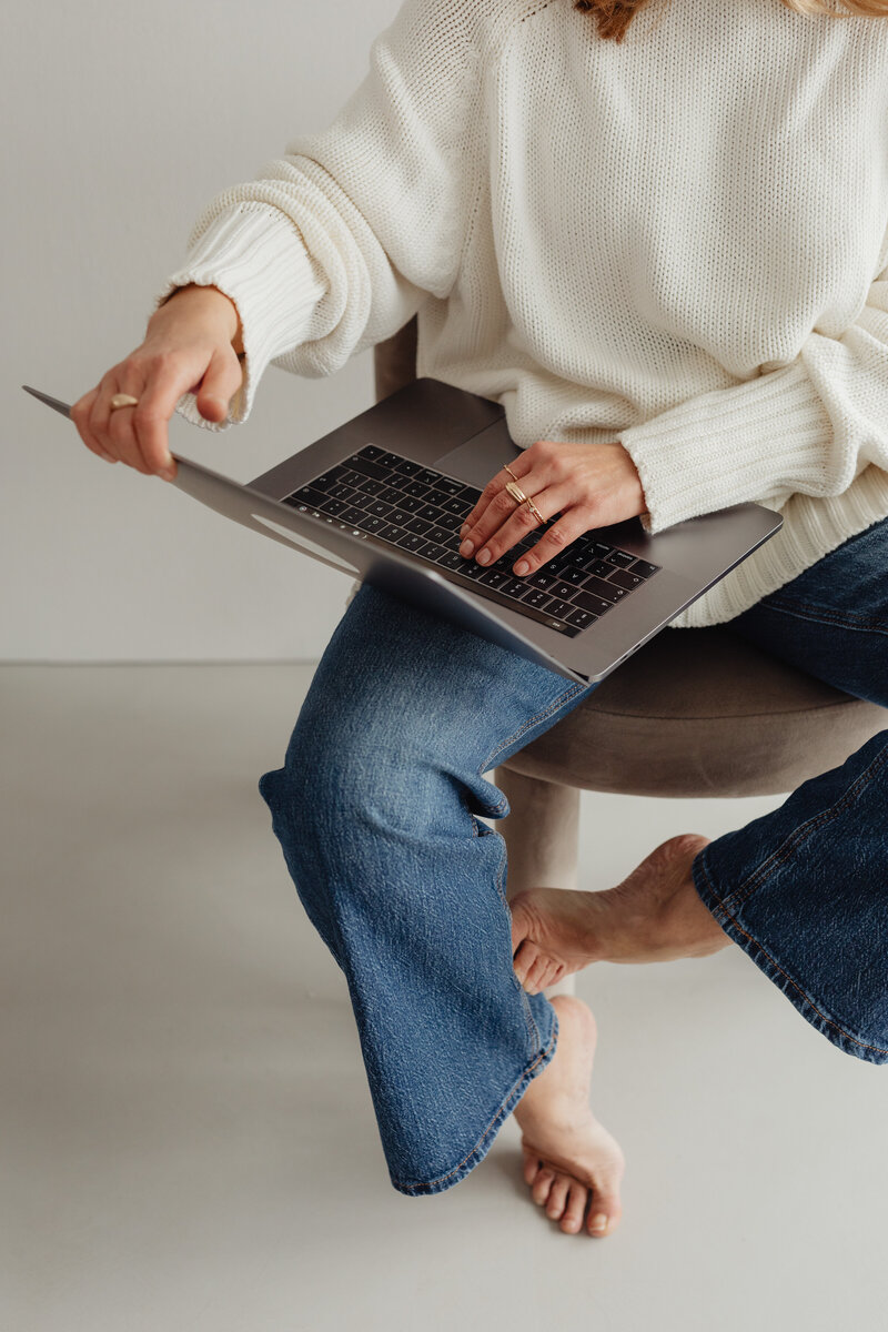 Woman in white sweater and jeans holding laptop