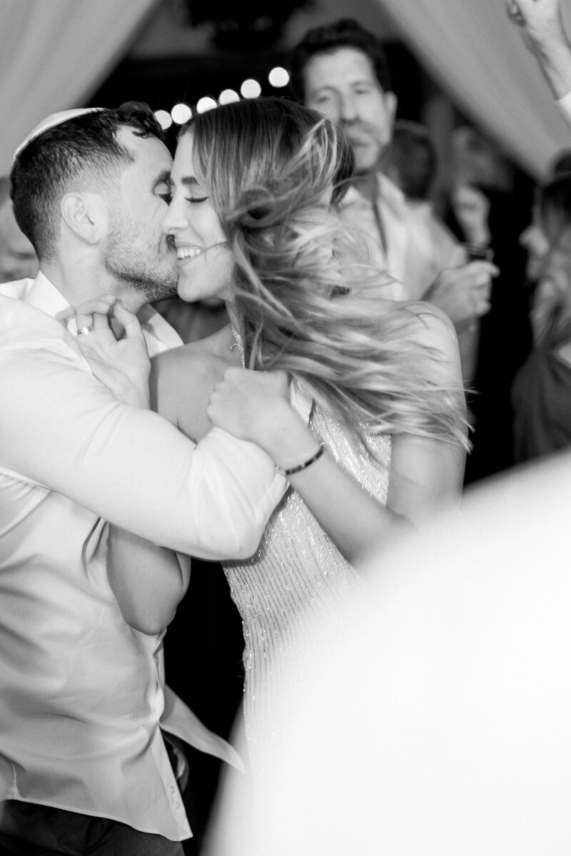 Groom kisses his smiling bride as they dance at their wedding reception