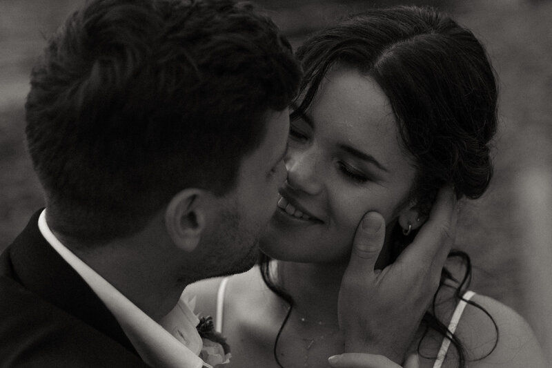 Close up black and white photo of bride and groom going in for a kiss with emphasis on the brides face 